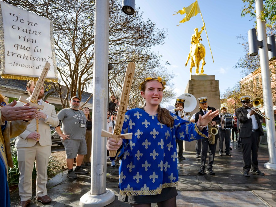 A procession of Krewe de Jeanne d'Arc represented by 2025 Maid of Honor Life Sacco, center, and the Soul Heirs Brass Band dances by a golden statue of St. Joan of Arc in the French Quarter after leaving St. Louis Cathedral in New Orleans, Sunday, Jan. 5, 2025, after a mass honoring victims of the New Year's Day deadly truck attack and shooting not far from the cathedral in the French Quarter. (AP Photo/Matthew Hinton)