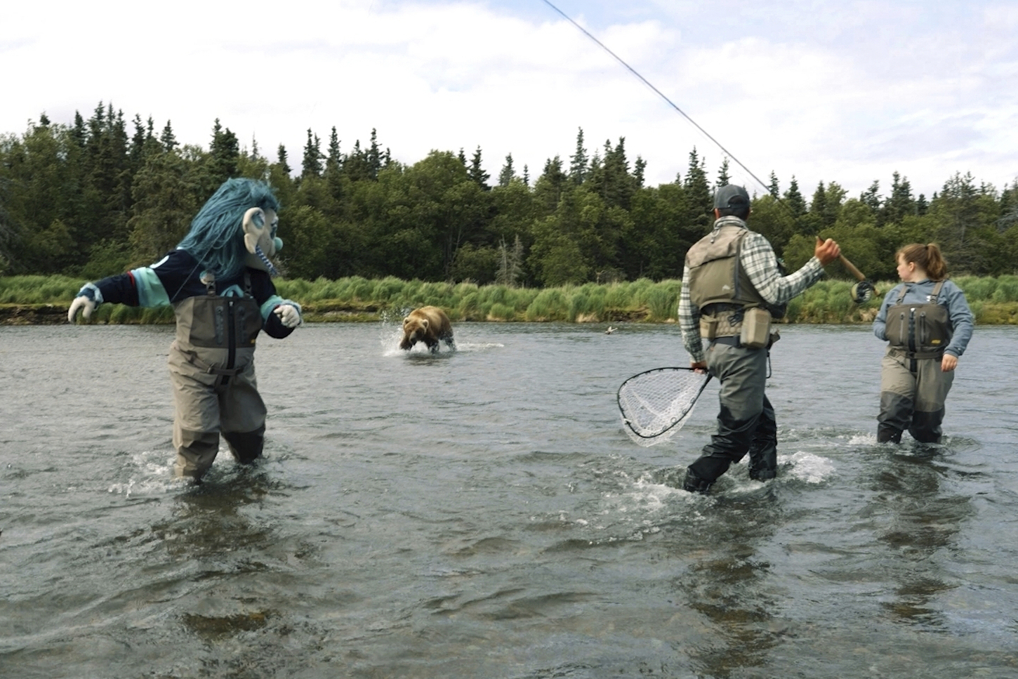 This image taken from video provided by the Seattle Kraken shows a brown bear splashing toward the NHL Kraken sea troll mascot known as Buoy, left, next to a fishing guide during the filming of a promotional video in a river outside Anchorage, Alaska, June 25, 2025. (Seattle Kraken via AP)