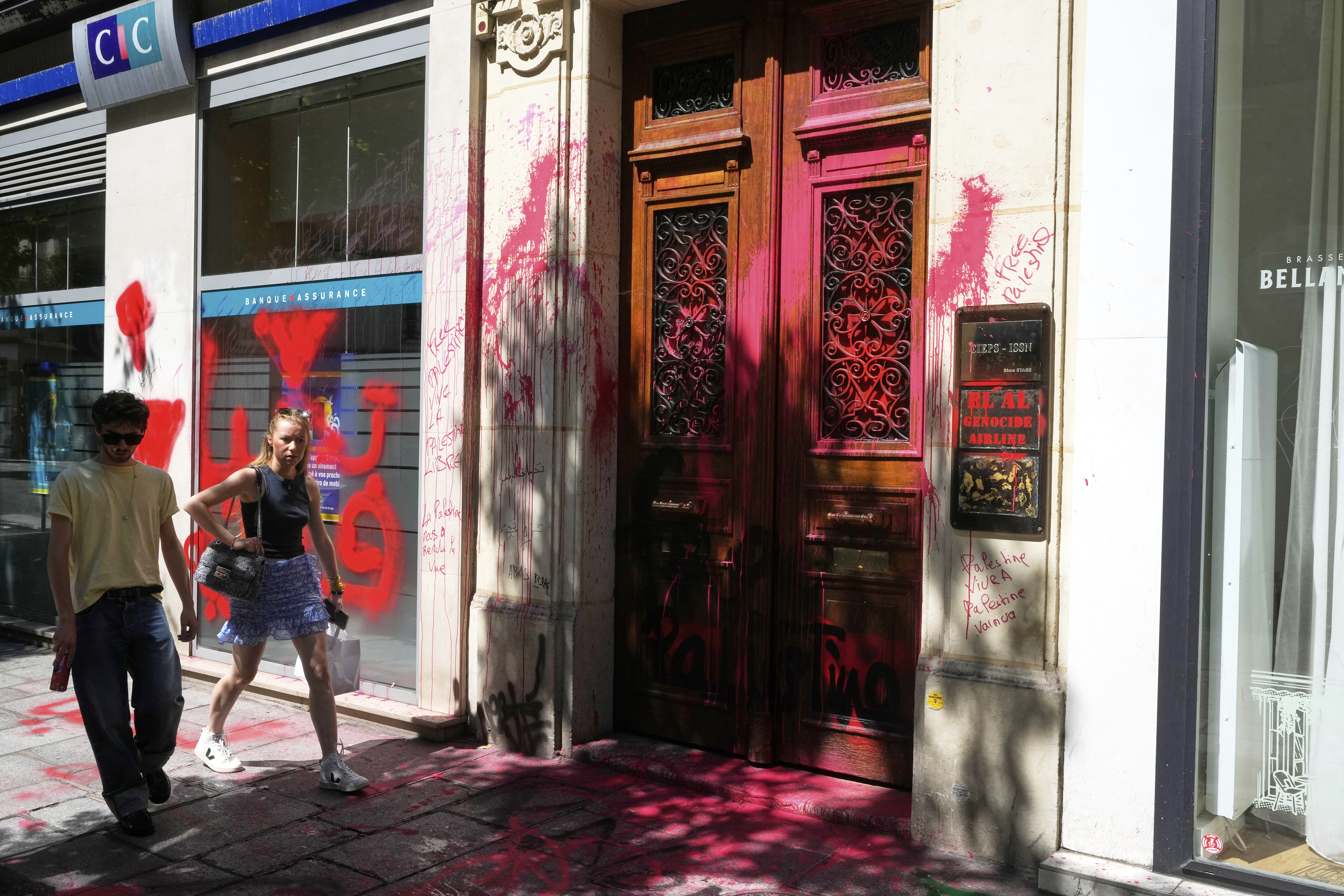People walk by the vandalized Israeli airline El Al Paris office, with anti-Israel graffiti, Thursday, Aug. 7, 2025 in Paris. (AP Photo/Michel Euler)