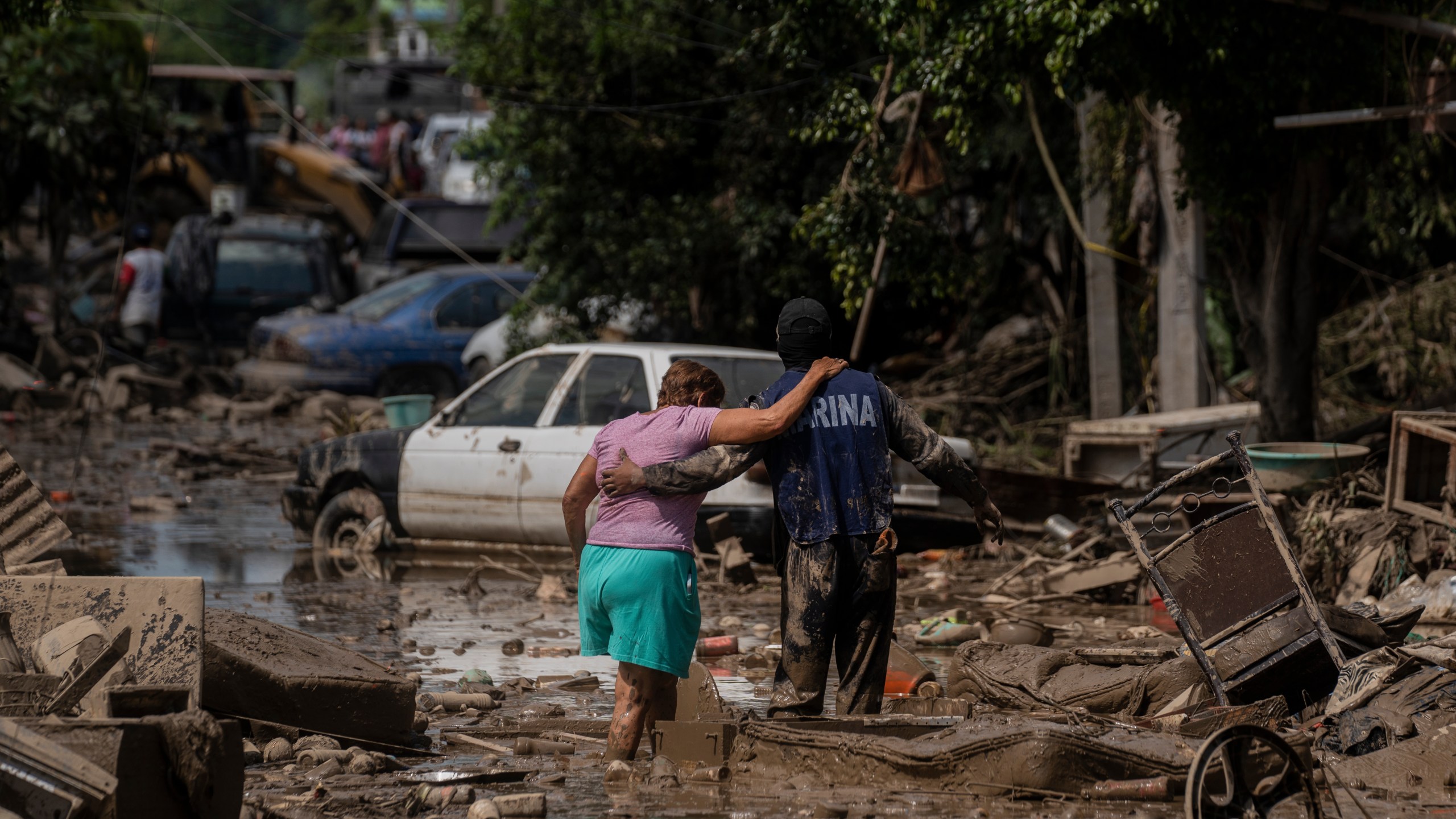 A Marine helps a woman cross a flooded street in Poza Rica, Veracruz state, Mexico, Sunday, Oct. 12, 2025. (AP Photo/Felix Marquez)