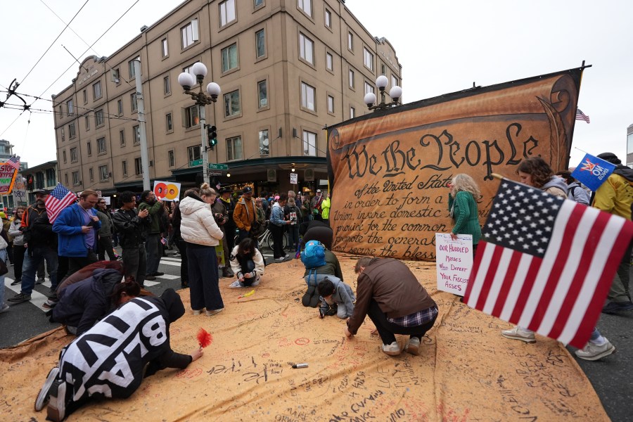 People are signing a giant Constitution as they take part in a "No Kings" protest Saturday, Oct. 18, 2025, in Seattle. (AP Photo/Lindsey Wasson)
