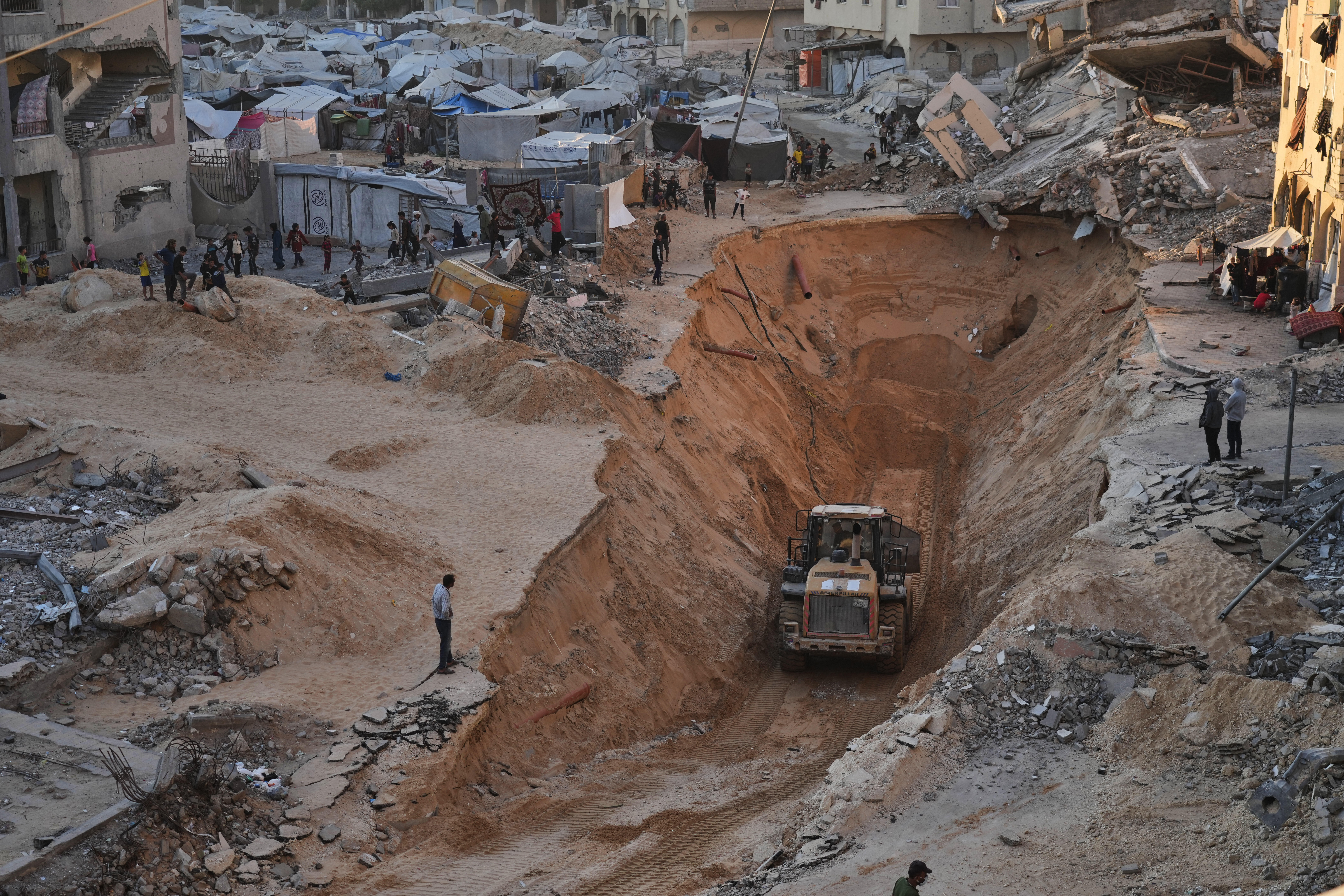 Palestinians watch members of the Hamas militant group searching for bodies of the hostages in Khan Younis, southern Gaza Strip, Saturday, Oct. 18, 2025. (AP Photo/Jehad Alshrafi)