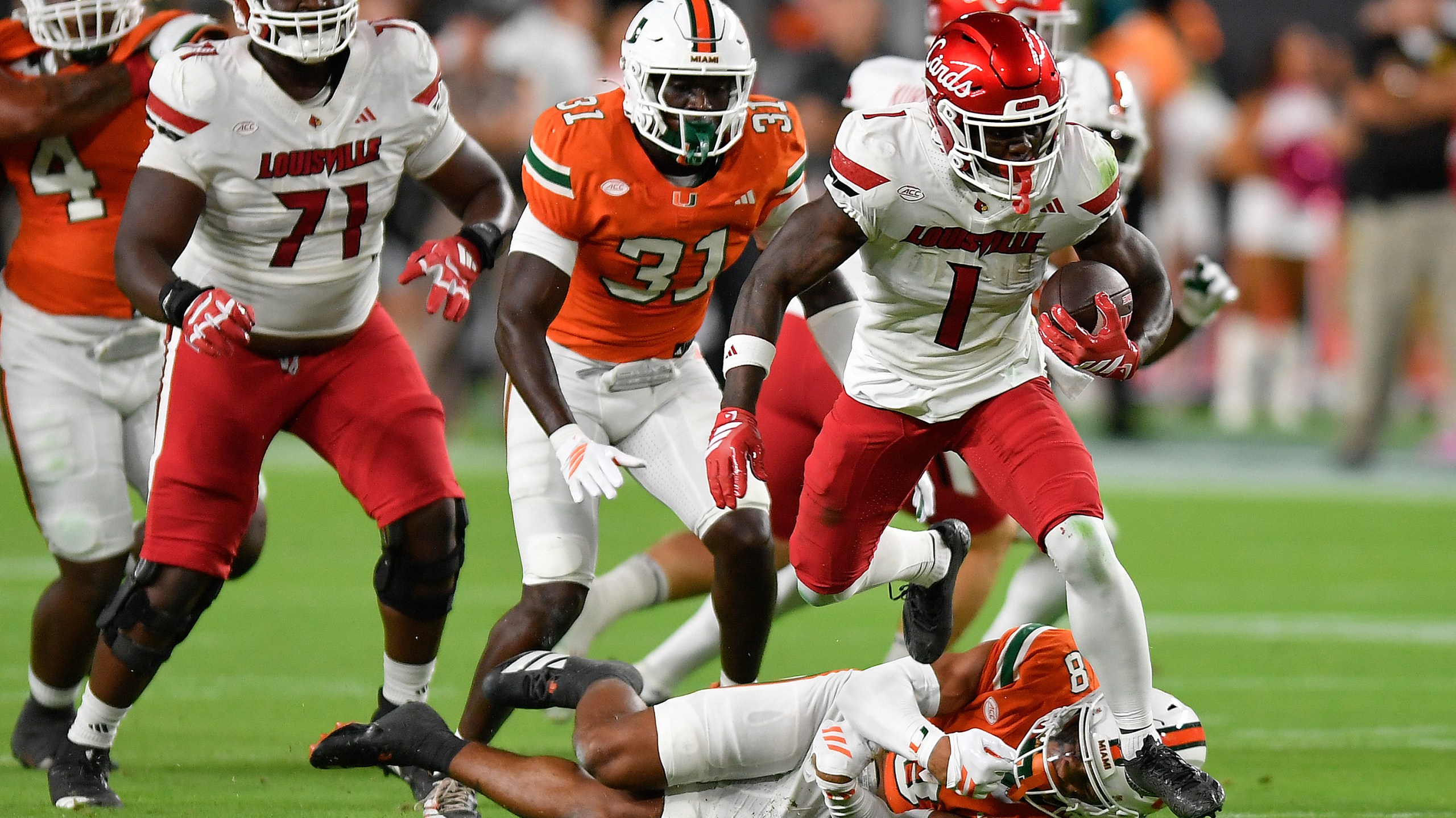 Louisville running back Isaac Brown (1) runs over Miami defensive back Jakobe Thomas (8) during the first half of an NCAA college football game, Friday, Oct. 17, 2025, in Miami Gardens, Fla. (AP Photo/Michael Laughlin)