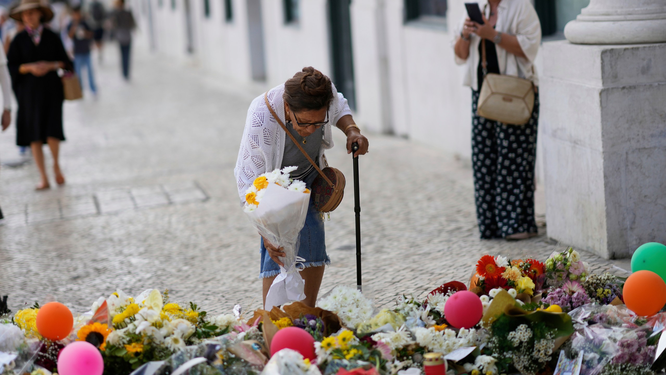 FILE - An elderly woman places a bouquet of flowers at a tribute to those that perished in the Gloria funicular, a tourist streetcar that derailed and crashed, in Lisbon, Sept. 6, 2025. (AP Photo/Armando Franca, File)