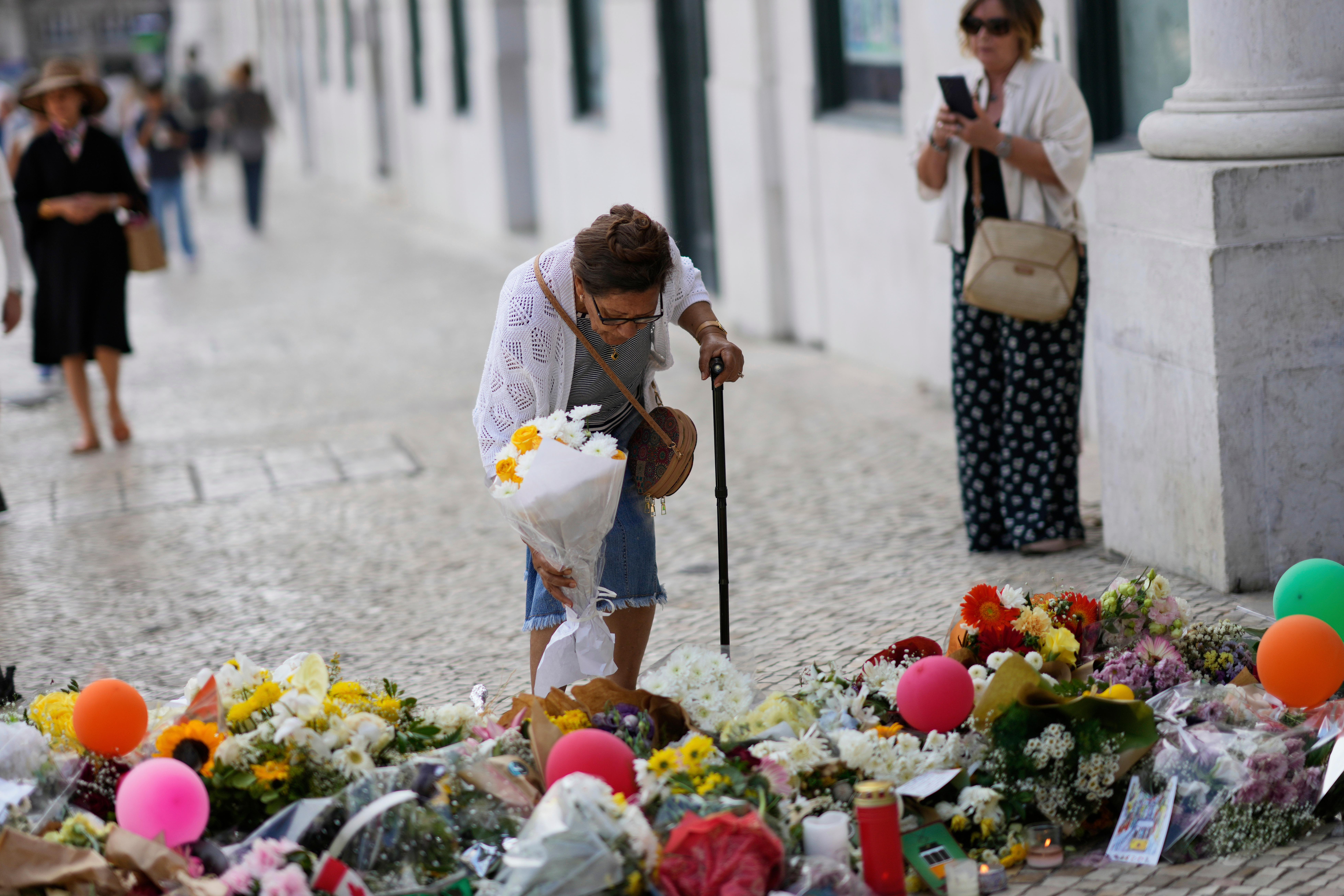 FILE - An elderly woman places a bouquet of flowers at a tribute to those that perished in the Gloria funicular, a tourist streetcar that derailed and crashed, in Lisbon, Sept. 6, 2025. (AP Photo/Armando Franca, File)