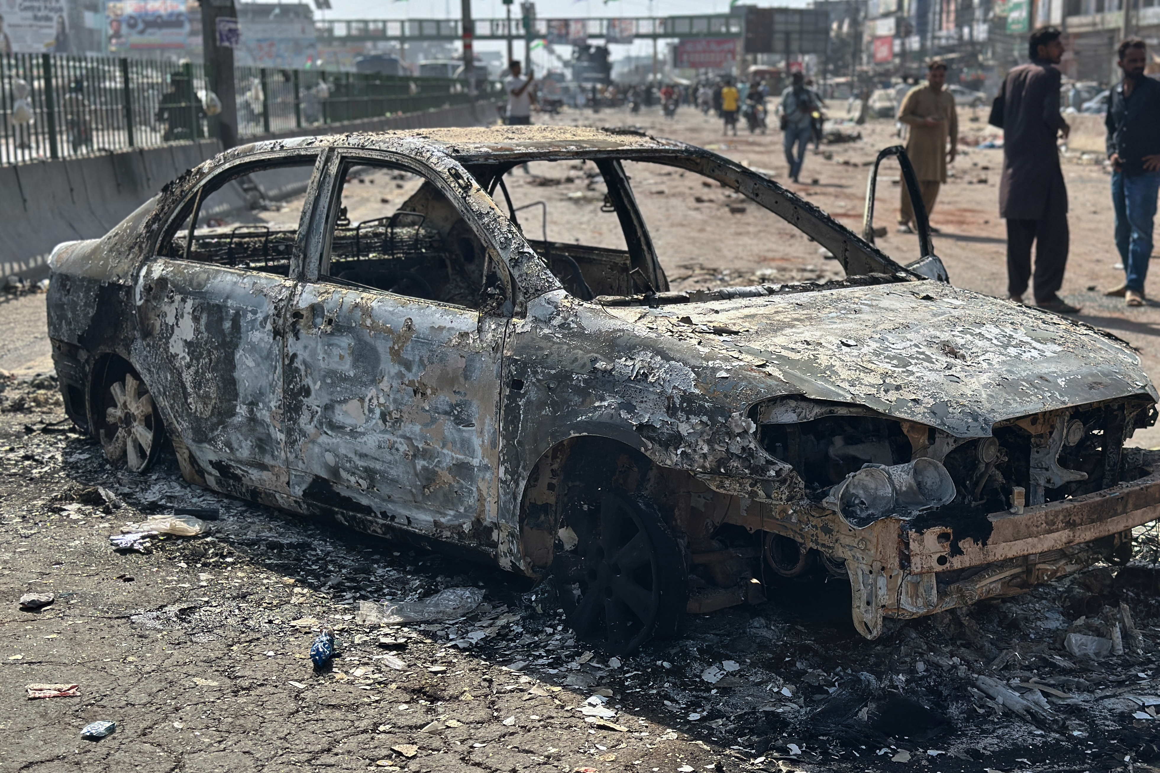 Local residents stand by burnt vehicles after police in Pakistan clashed with thousands of protesters during a march in support of Palestinians, in Muridke near Lahore, Pakistan, Monday, Oct. 13, 2025. (AP Photo/Jahanzeb Khan)