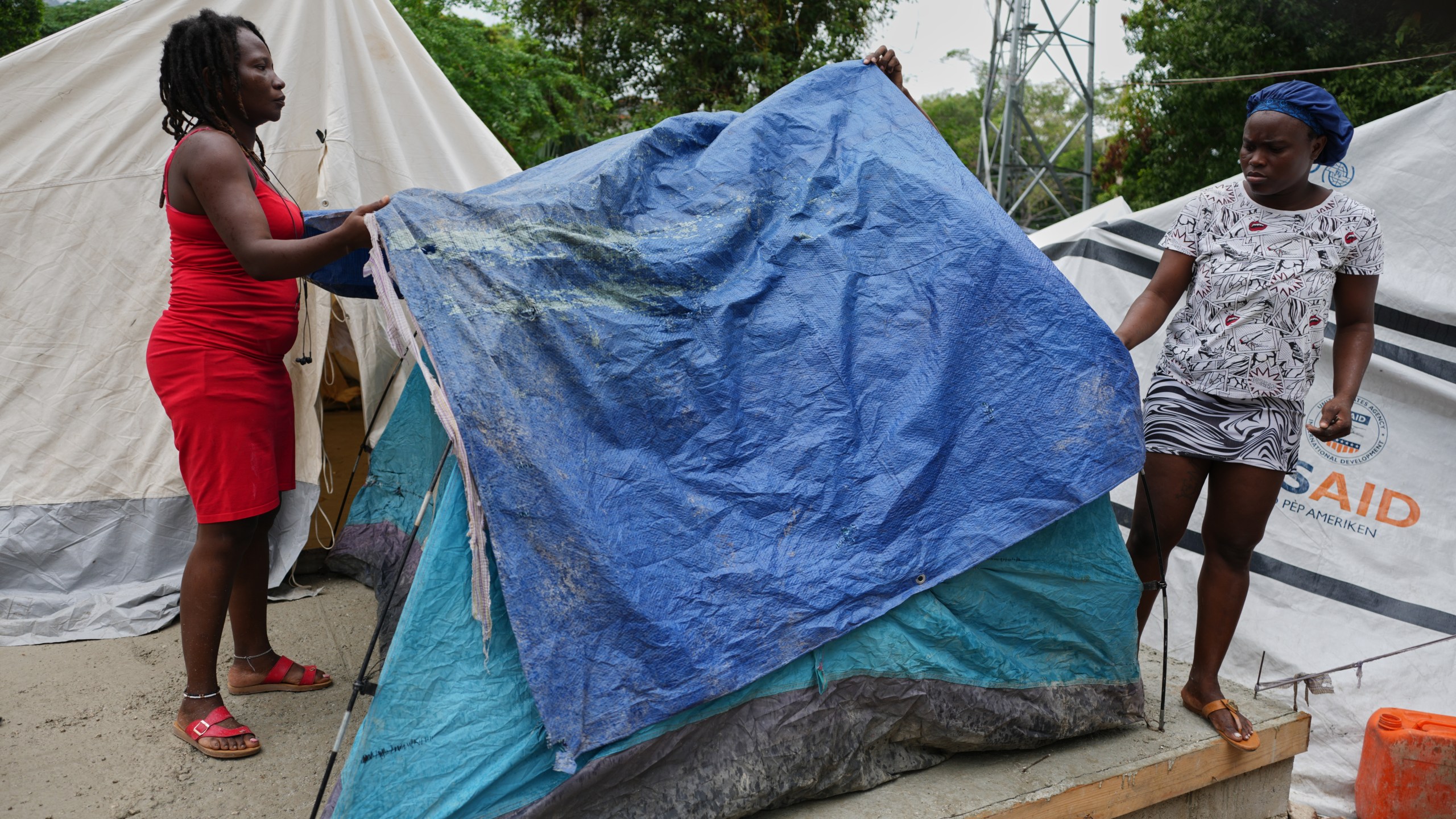 People place plastic tarps over their tents ahead of expected rain at a shelter for families displaced by gang violence in Port-au-Prince, Haiti, Thursday, Oct. 23, 2025. (AP Photo/Odelyn Joseph)