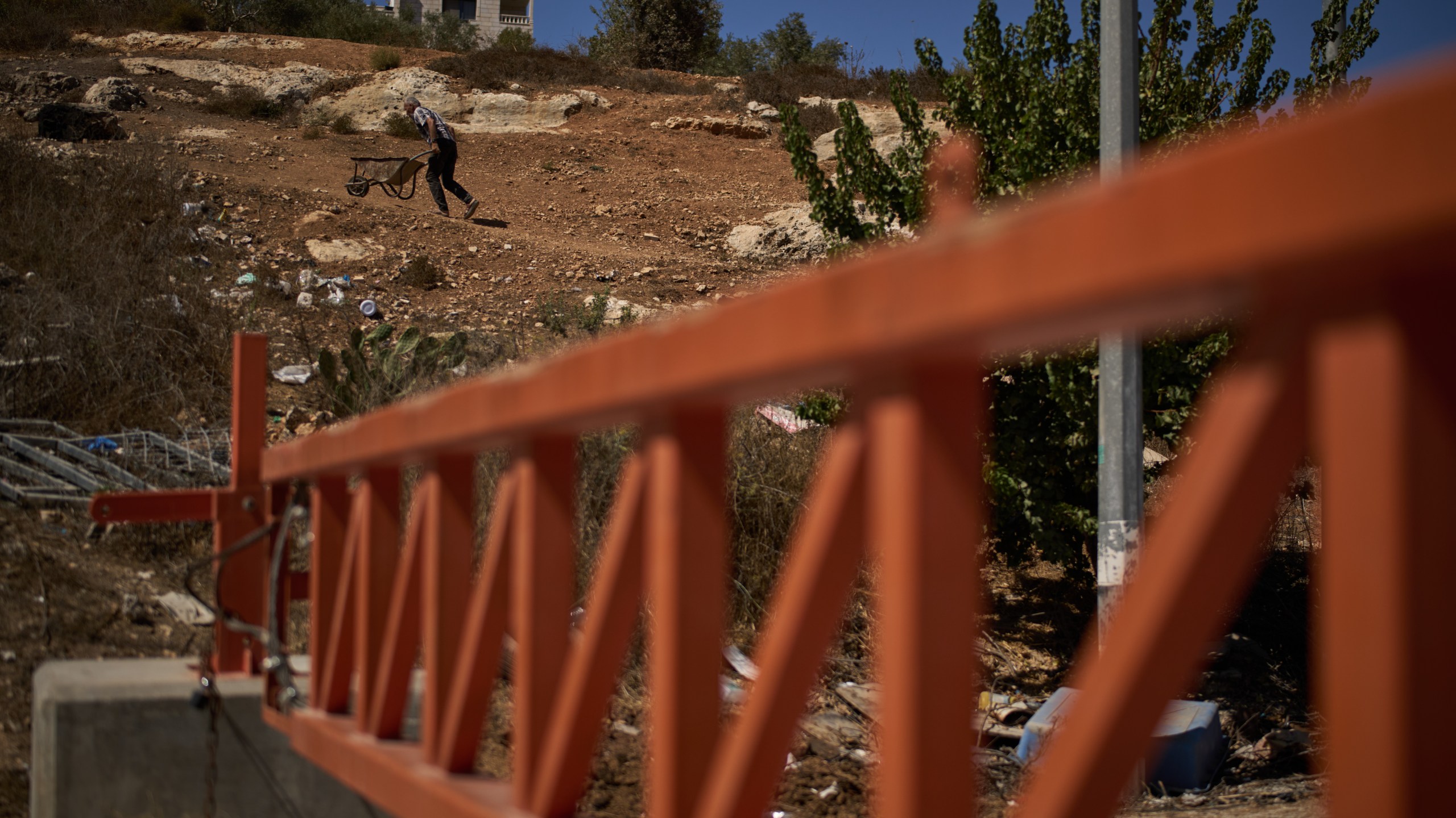 A Palestinian man pushes a wheelbarrow past a closed gate set up by Israeli authorities that blocks an entrance to the West Bank village of Sinjil, Tuesday, Sept. 30, 2025. (AP Photo/Leo Correa)