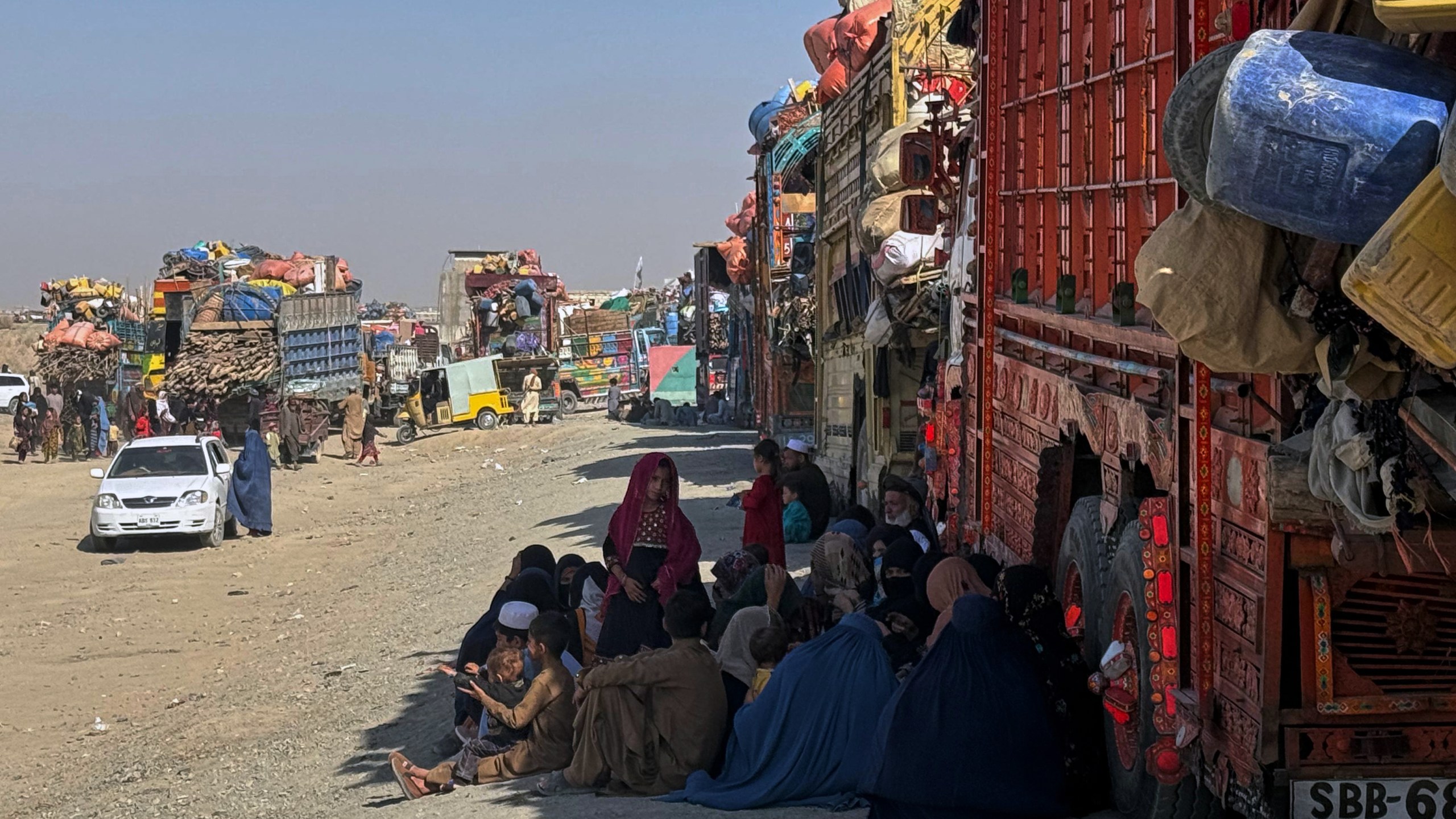 Afghan refugees sit beside trucks loaded with their belongings as they wait their turn to leave for their homeland through a border crossing point which partially opens following Oct.19 ceasefire on the outskirts of Chaman, a border town on the Pakistan Afghan border, Wednesday, Oct. 29, 2025. (AP Photo/H. Achakzai)