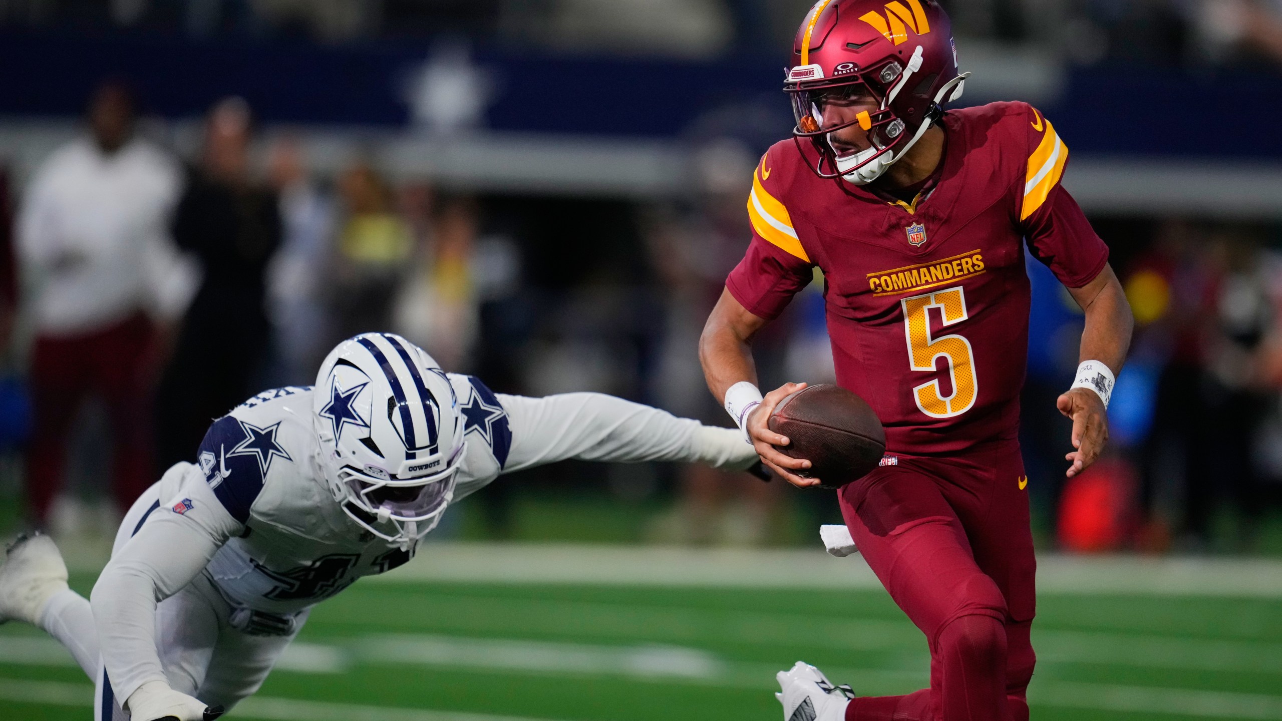 Washington Commanders quarterback Jayden Daniels (5) avoids a tackle by Dallas Cowboys defensive end Donovan Ezeiruaku during the first half of an NFL football game Sunday, Oct. 19, 2025, in Arlington, Texas. (AP Photo/Jeffrey McWhorter)