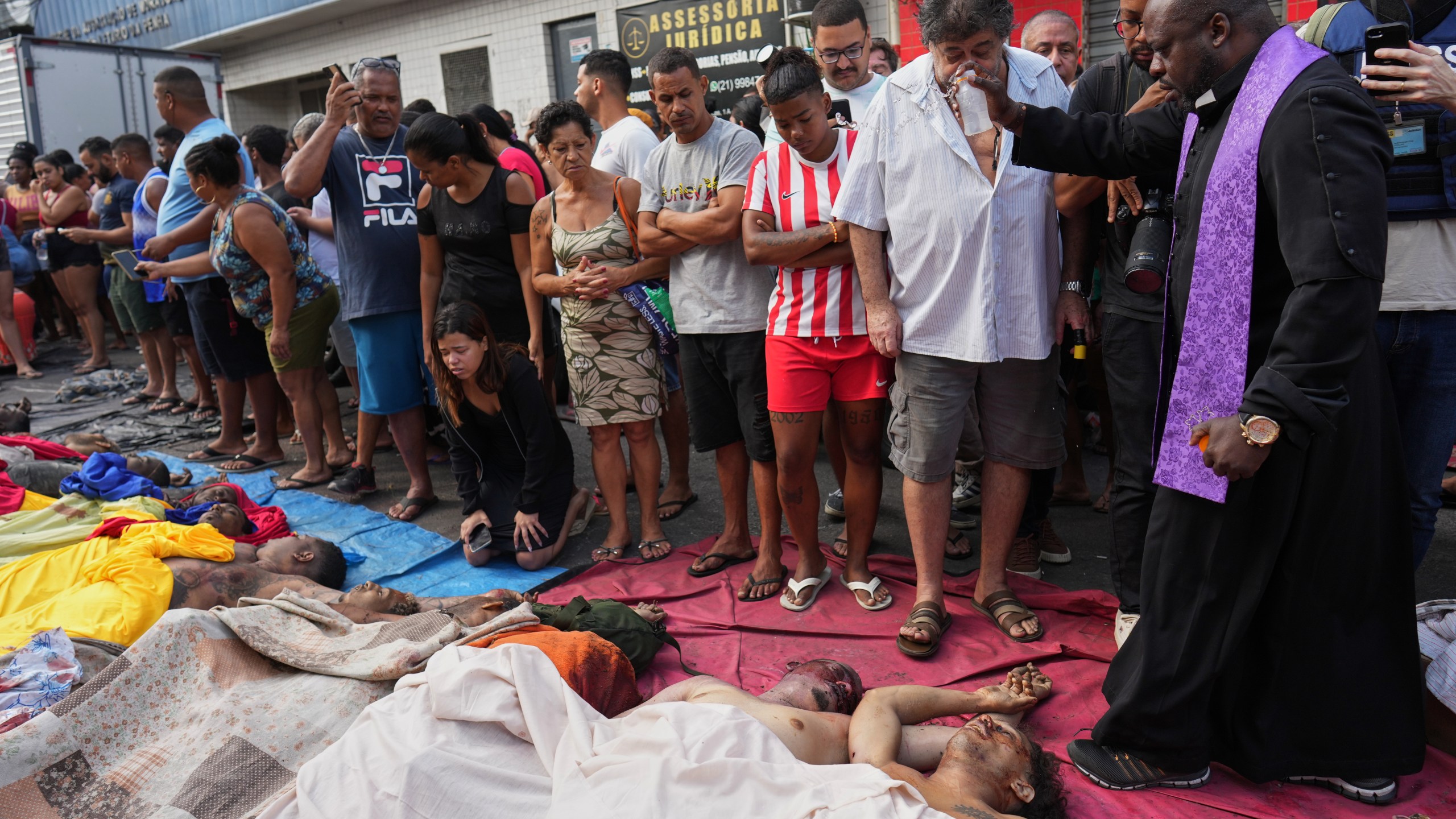 A priest blesses the bodies of people killed the day before during a police raid targeting the Comando Vermelho gang in the Complexo da Penha favela of Rio de Janeiro, Brazil, Wednesday, Oct. 29, 2025. (AP Photo/Silvia Izquierdo)