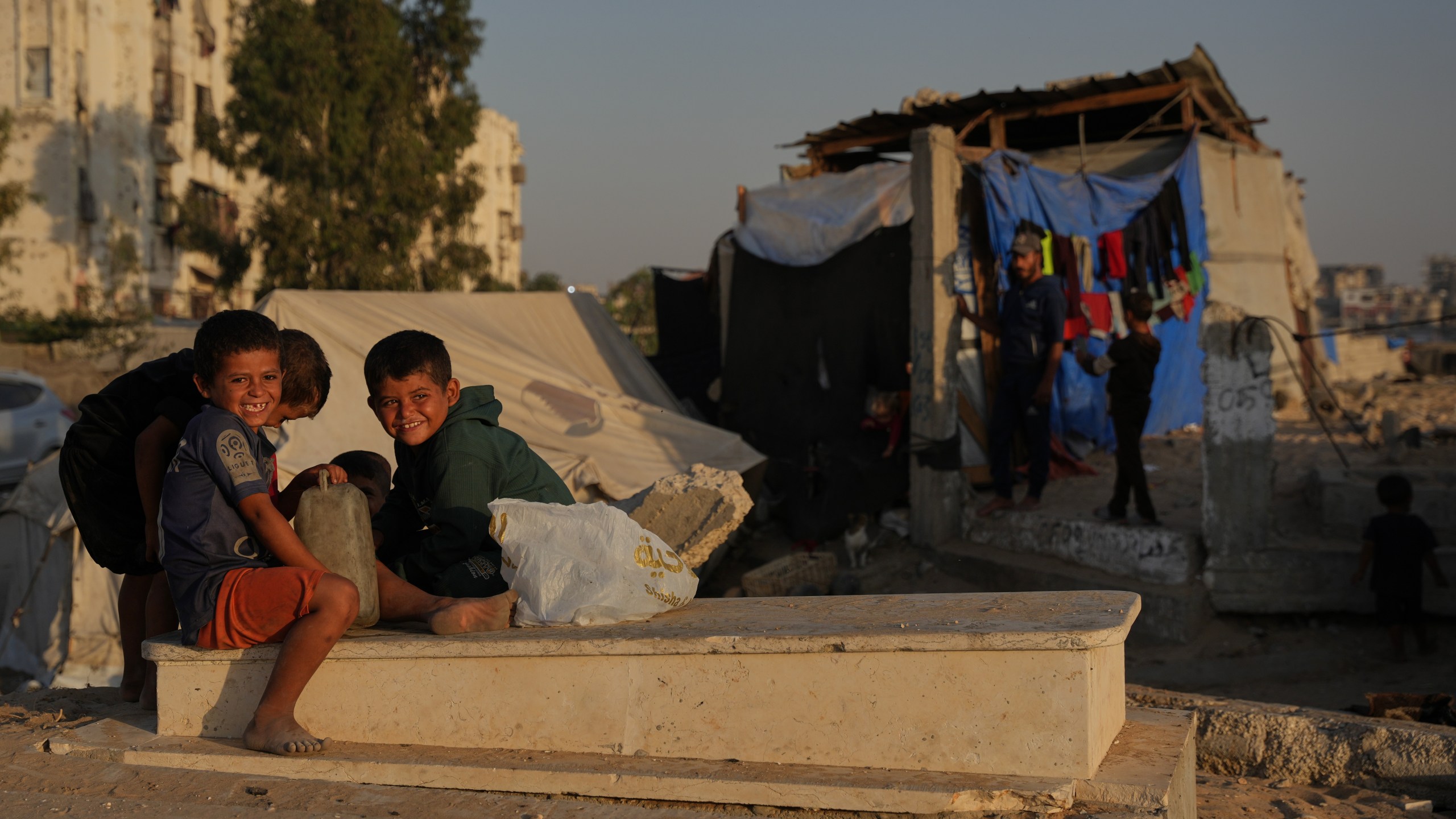 Palestinian children sit on a grave near makeshift tents for displaced people that were set up in a cemetery in Khan Younis, in the southern Gaza Strip, Friday, Oct. 31, 2025. (AP Photo/Abdel Kareem Hana)