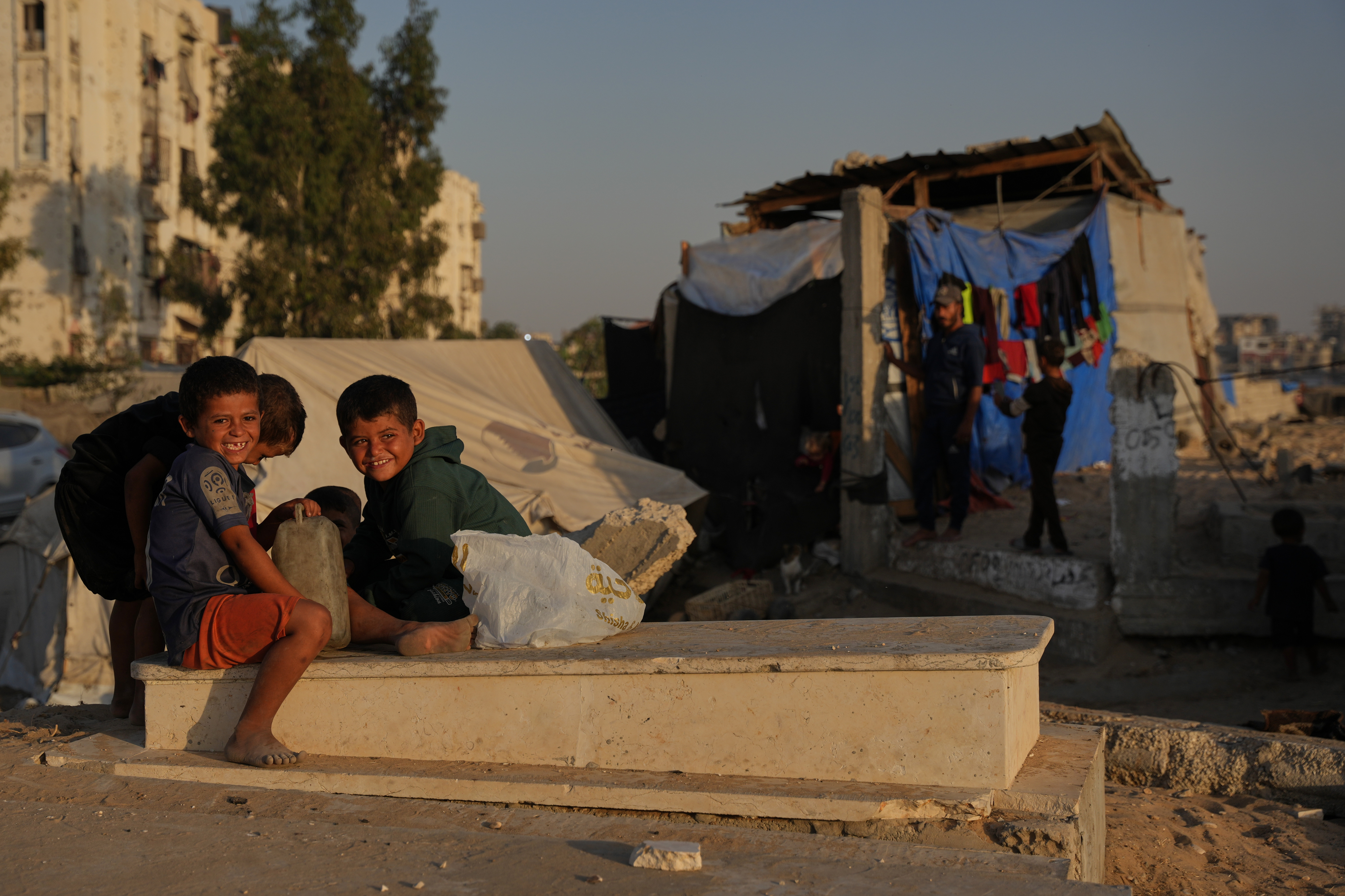 Palestinian children sit on a grave near makeshift tents for displaced people that were set up in a cemetery in Khan Younis, in the southern Gaza Strip, Friday, Oct. 31, 2025. (AP Photo/Abdel Kareem Hana)