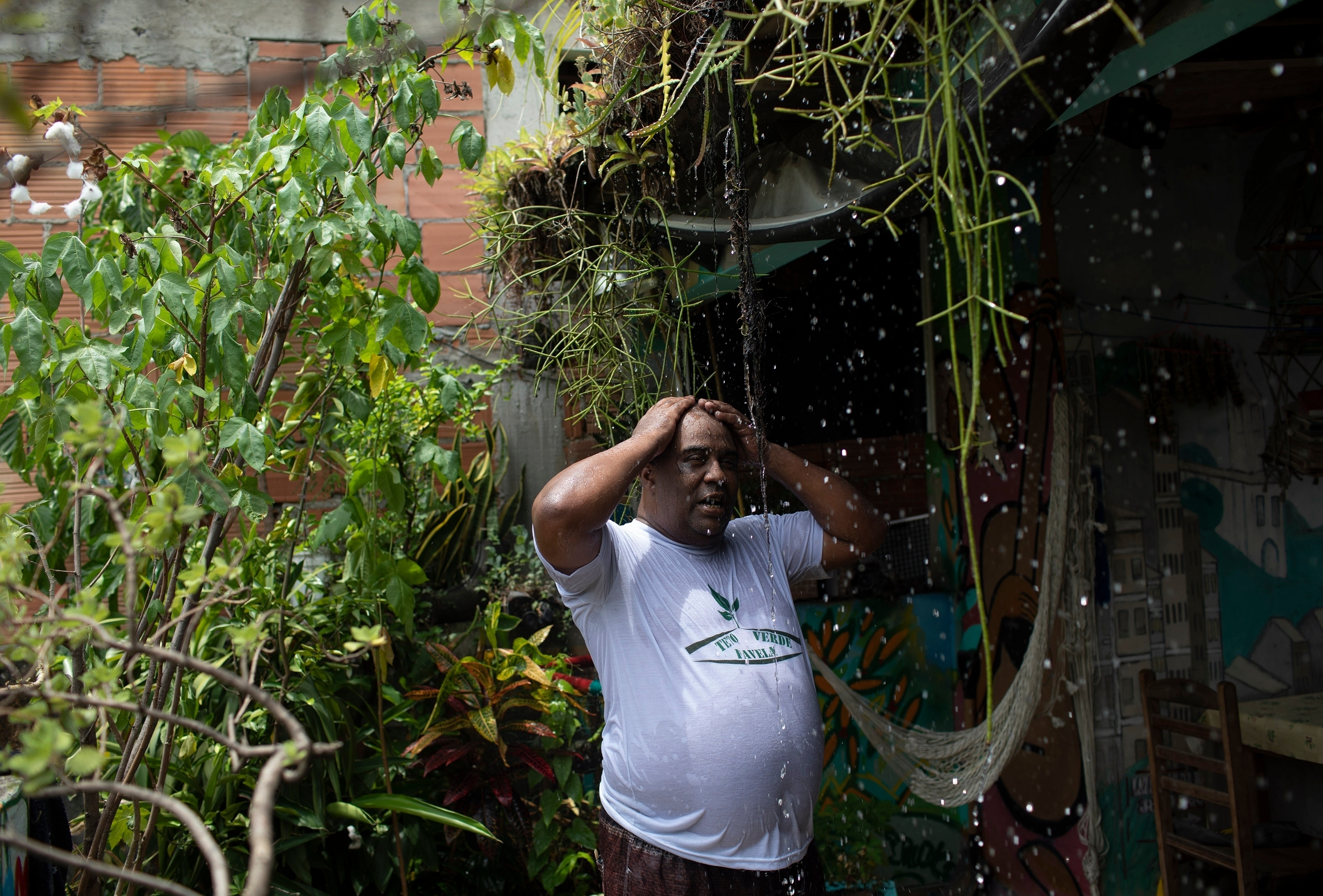 FILE - Luis Cassiano cools off with water that falls from his green roof at his home in Arara, a poor neighborhood, in Rio de Janeiro on Jan. 9, 2020. (AP Photo/Silvia Izquierdo, File)