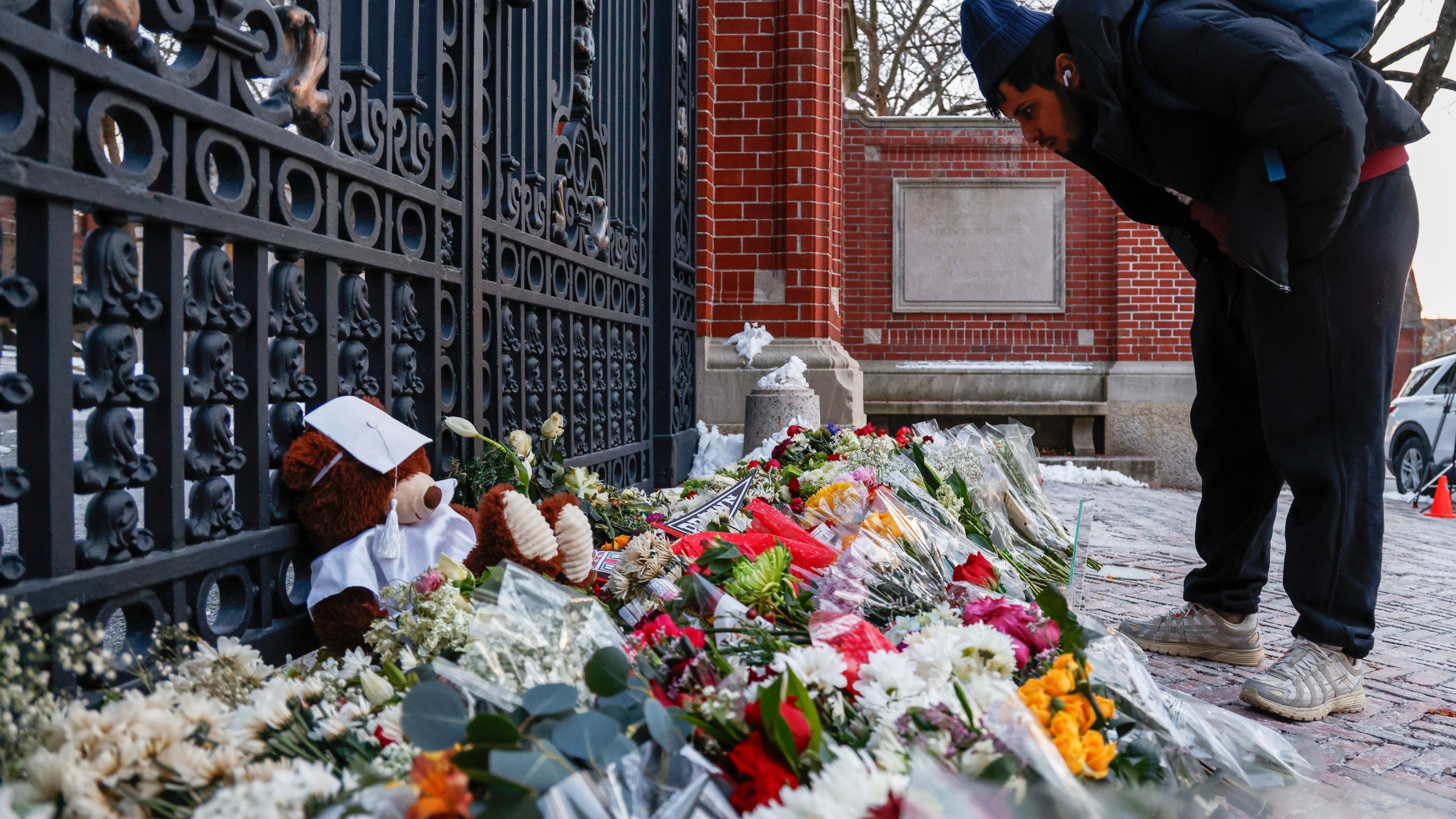 A community member looks at flowers, notes and mementos in a makeshift memorial display sitting in front of Brown University's Van Wickle gates, in Providence, R.I., two days after a shooting took place on the university's campus, Monday, Dec. 15, 2025. (Lily Speredelozzi/The Sun Chronicle via AP)