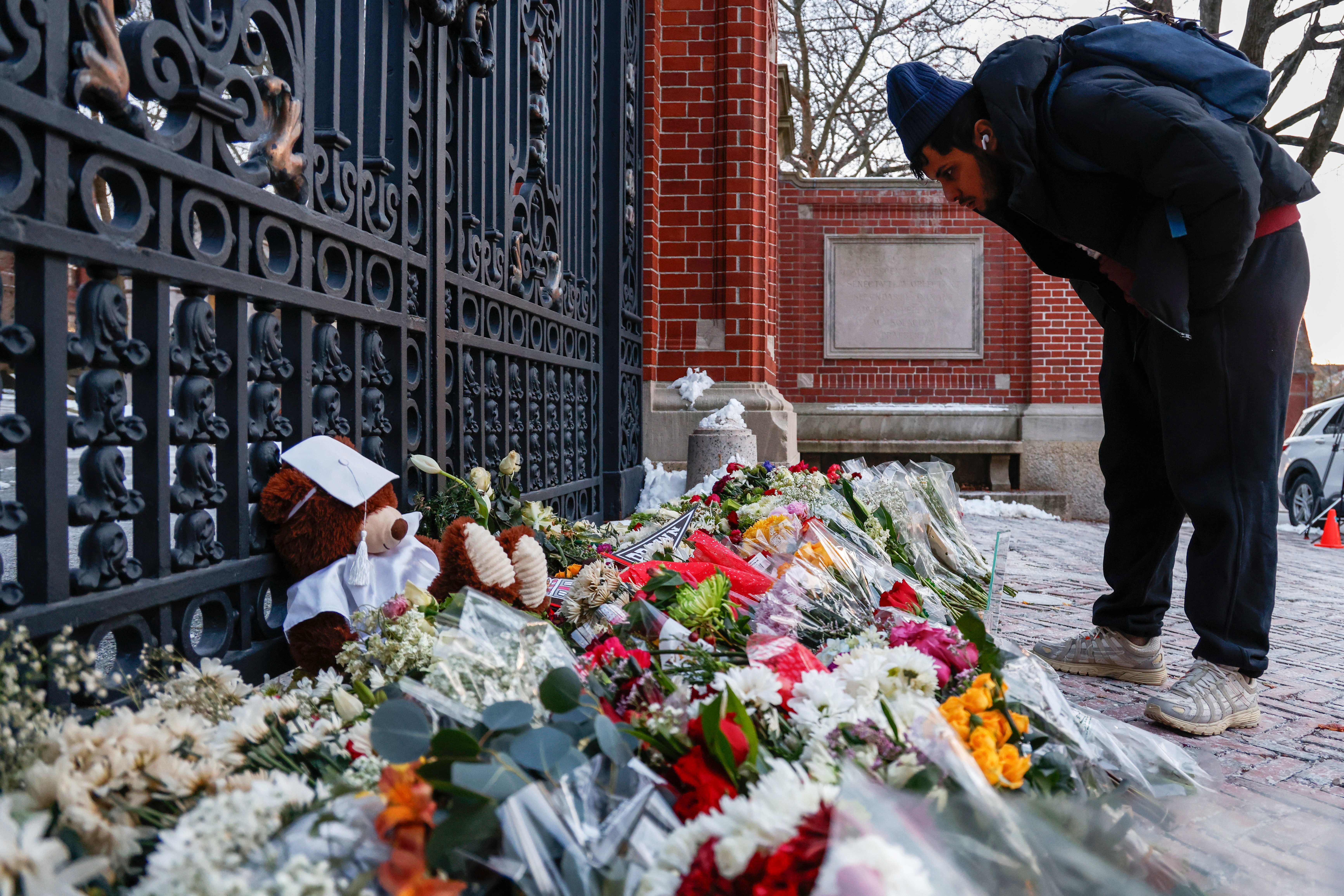 A community member looks at flowers, notes and mementos in a makeshift memorial display sitting in front of Brown University's Van Wickle gates, in Providence, R.I., two days after a shooting took place on the university's campus, Monday, Dec. 15, 2025. (Lily Speredelozzi/The Sun Chronicle via AP)