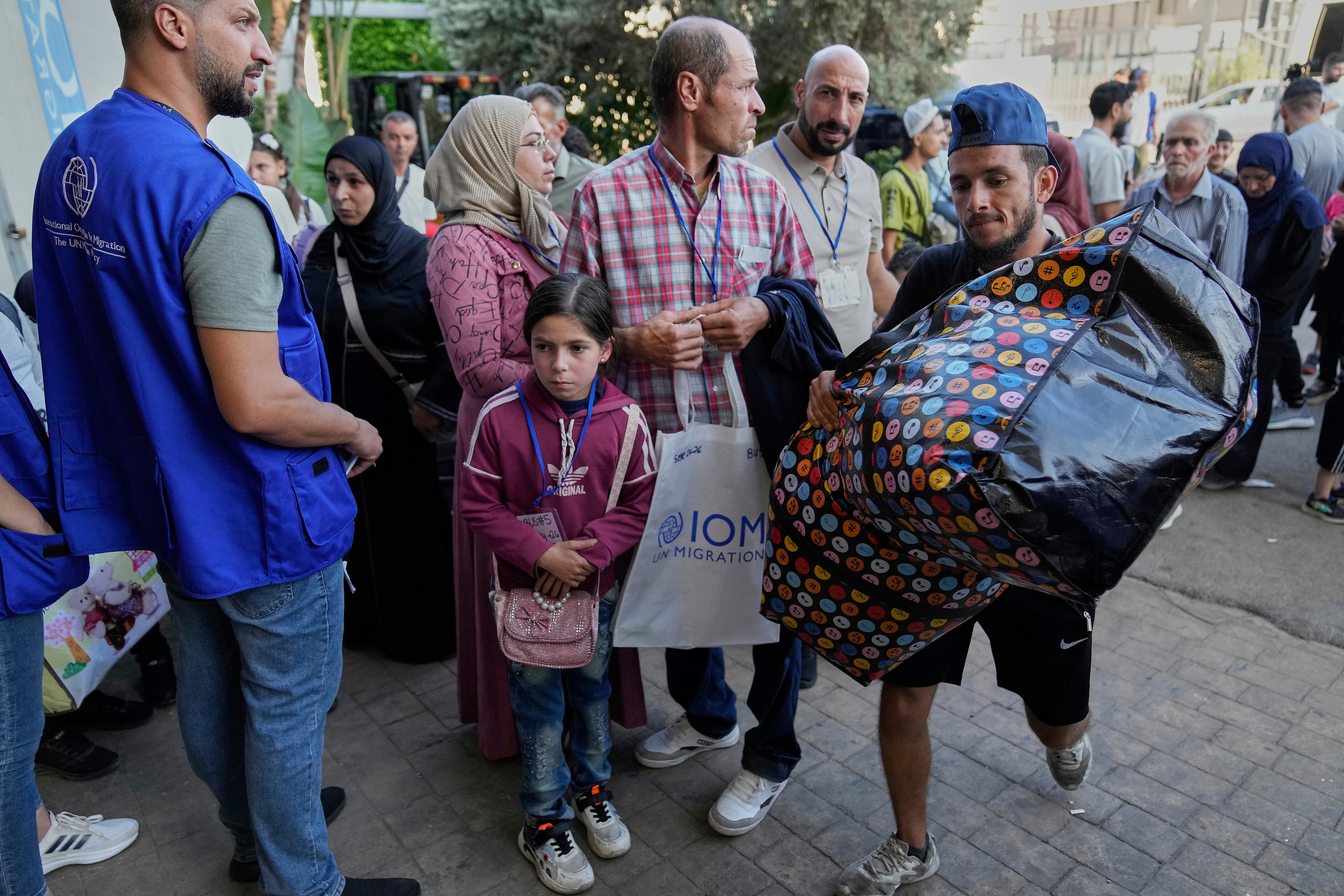 FILE - A worker, right, carries a bag as Syrian refugees line up at a gathering point to be checked by Lebanese security forces before they board buses to return home to Syria, in Beirut, Lebanon, Thursday, Sept. 11, 2025. (AP Photo/Hussein Malla, File)