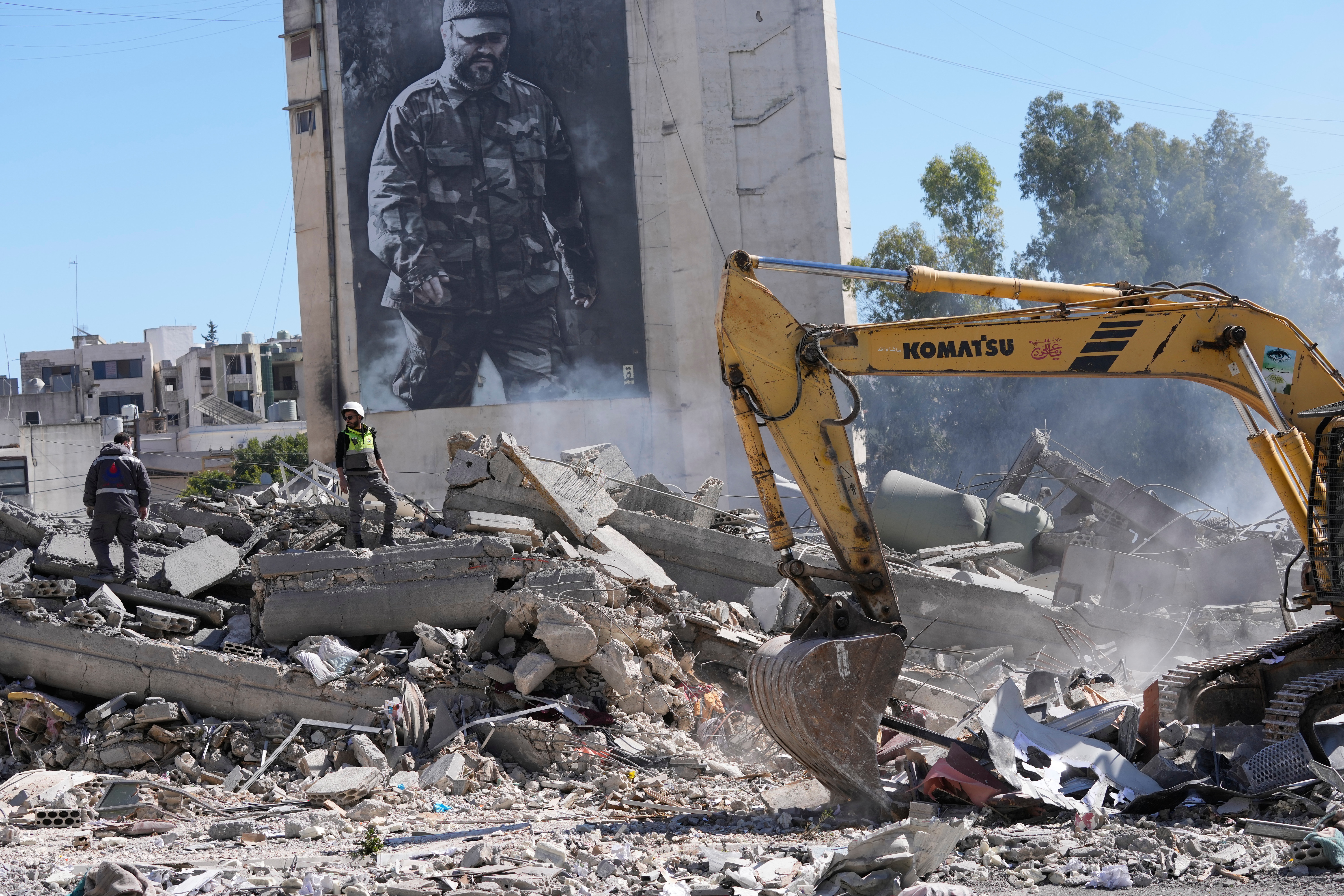 A giant poster shows the late Hezbollah military commander Imad Mughniyeh, while workers check a destroyed building that was hit by an Israeli airstrike in Nabatiyeh town, south Lebanon, Thursday, March 5, 2026. (AP Photo/Mohammed Zaatari)
